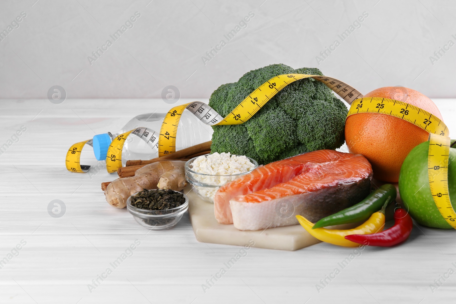 Photo of Metabolism. Different food products and measuring tape on white wooden table