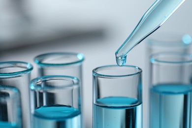 Photo of Dripping liquid from pipette into test tube on blurred background, closeup