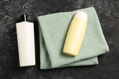 Photo of Soft folded terry towel and cosmetic bottles on black textured background, flat lay