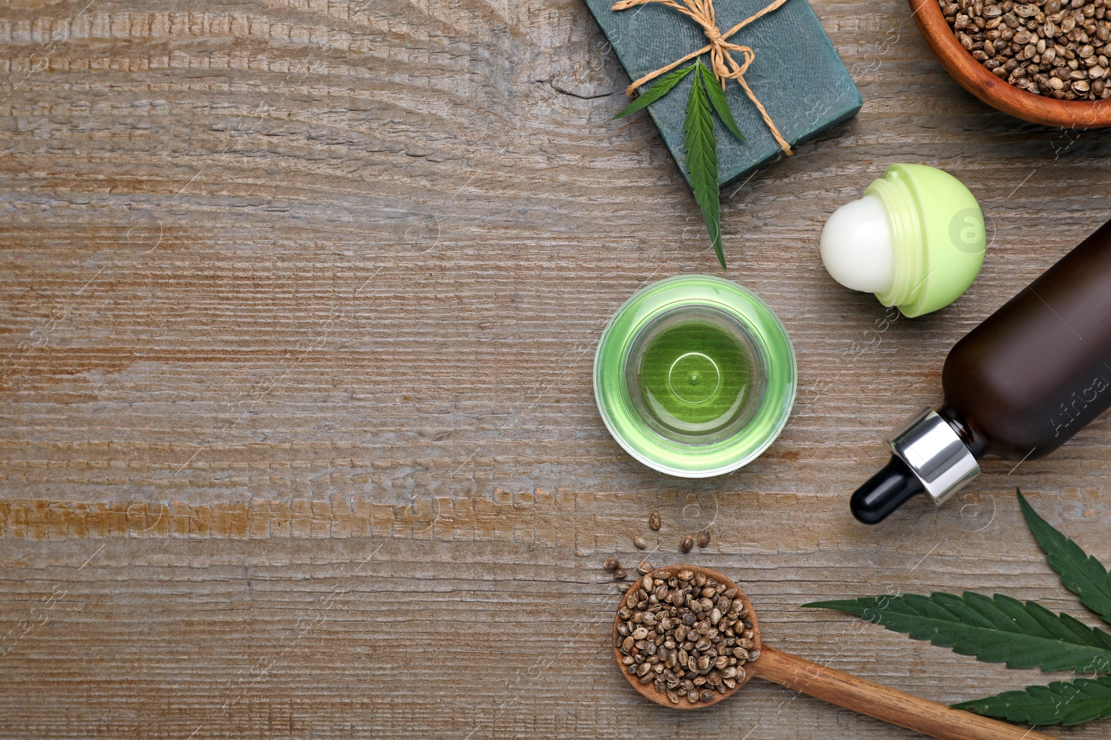 Photo of Hemp cosmetics and green leaves on wooden table, flat lay. Space for text