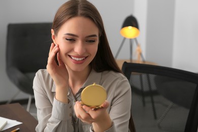 Young woman looking at herself in cosmetic pocket mirror indoors, space for text