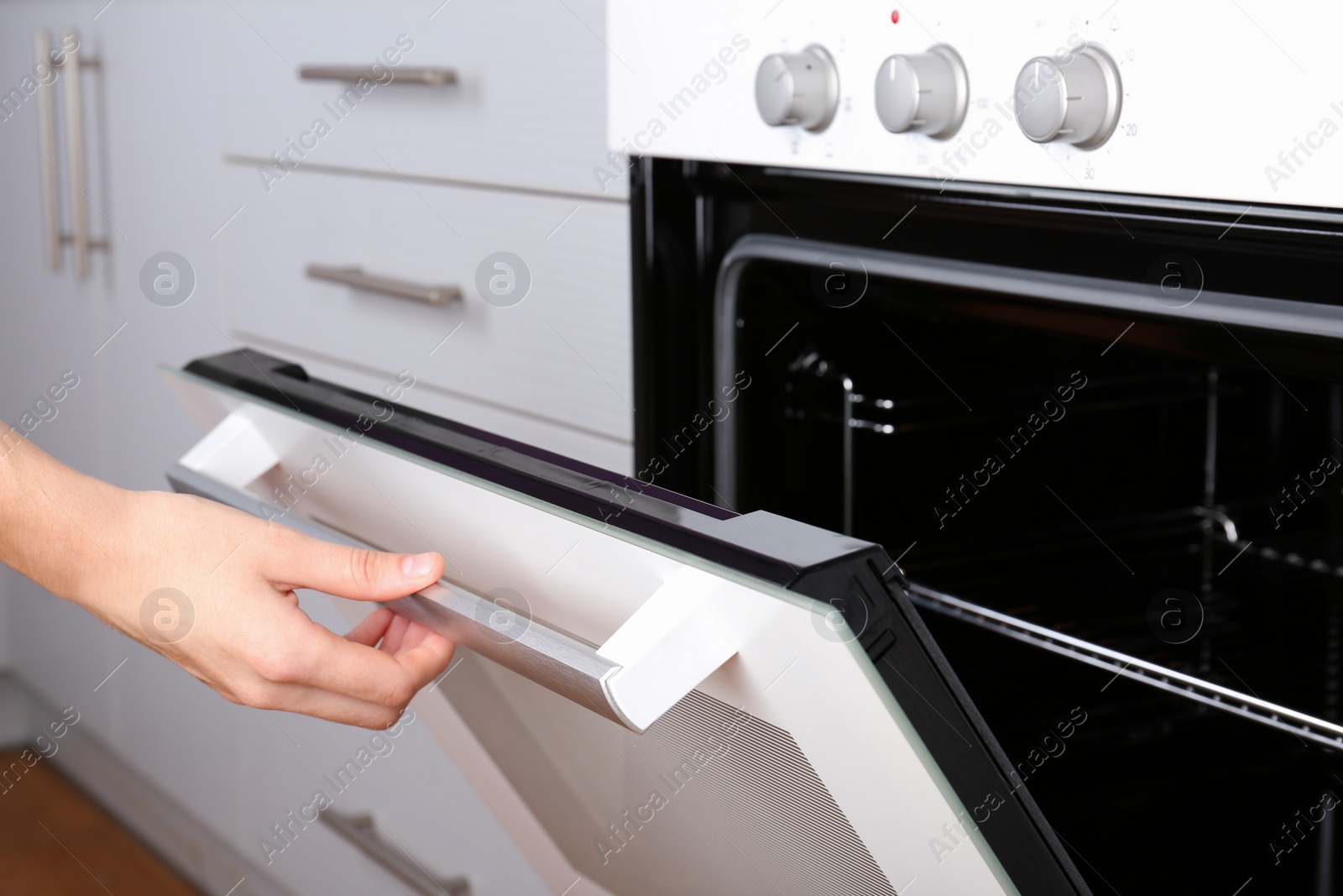 Photo of Woman opening electric oven in kitchen, closeup