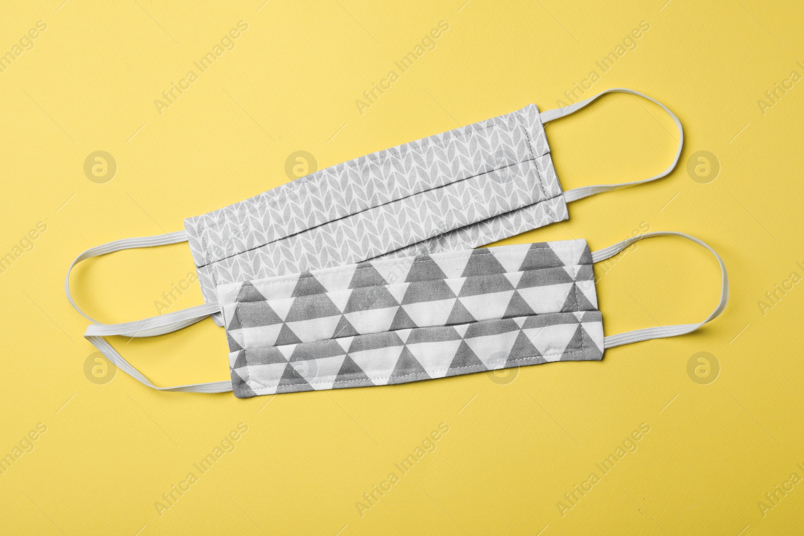 Photo of Homemade protective masks on yellow background, flat lay. Sewing idea