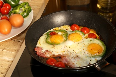 Cooking eggs with bacon, tomatoes and pepper in frying pan