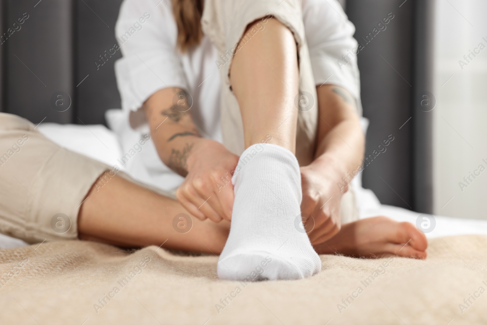 Photo of Woman putting on white socks in bedroom, closeup