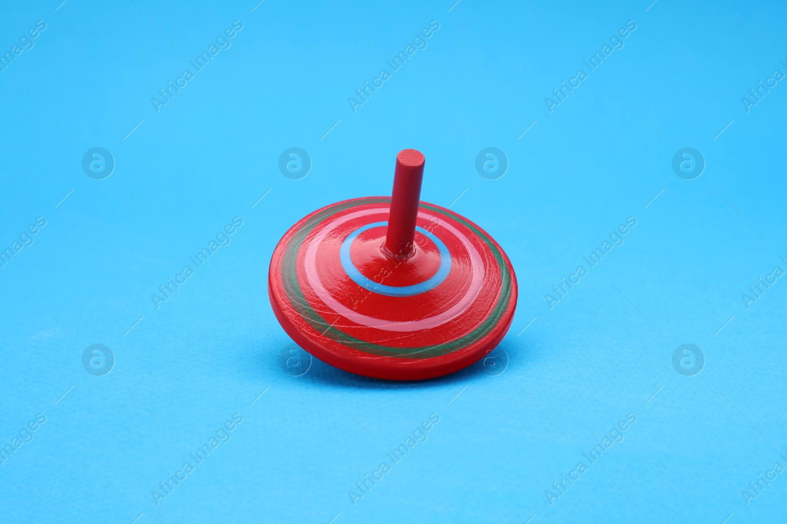 Photo of One bright spinning top on light blue background. Toy whirligig