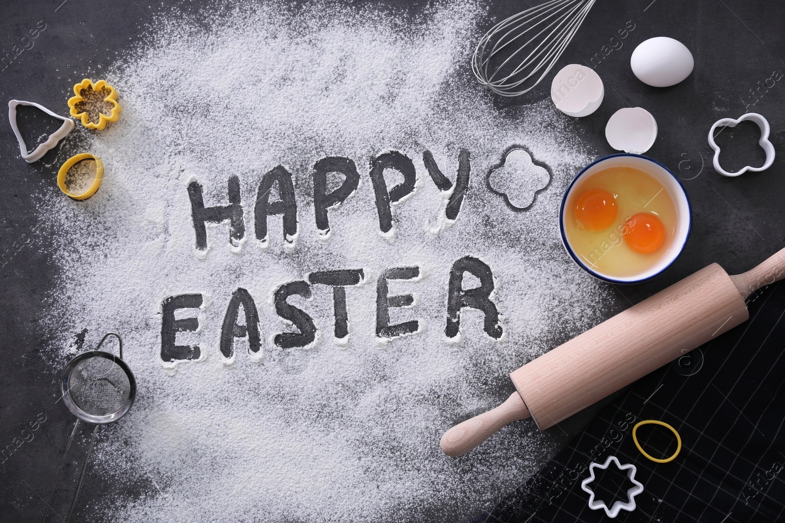 Photo of Cooking tools, ingredients for cake and words Happy Easter written in flour on black table, flat lay