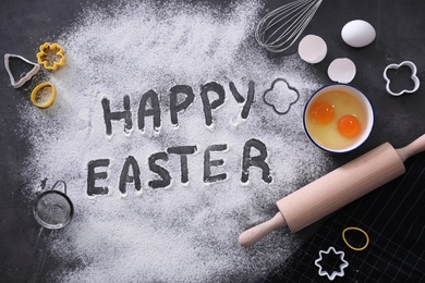 Photo of Cooking tools, ingredients for cake and words Happy Easter written in flour on black table, flat lay