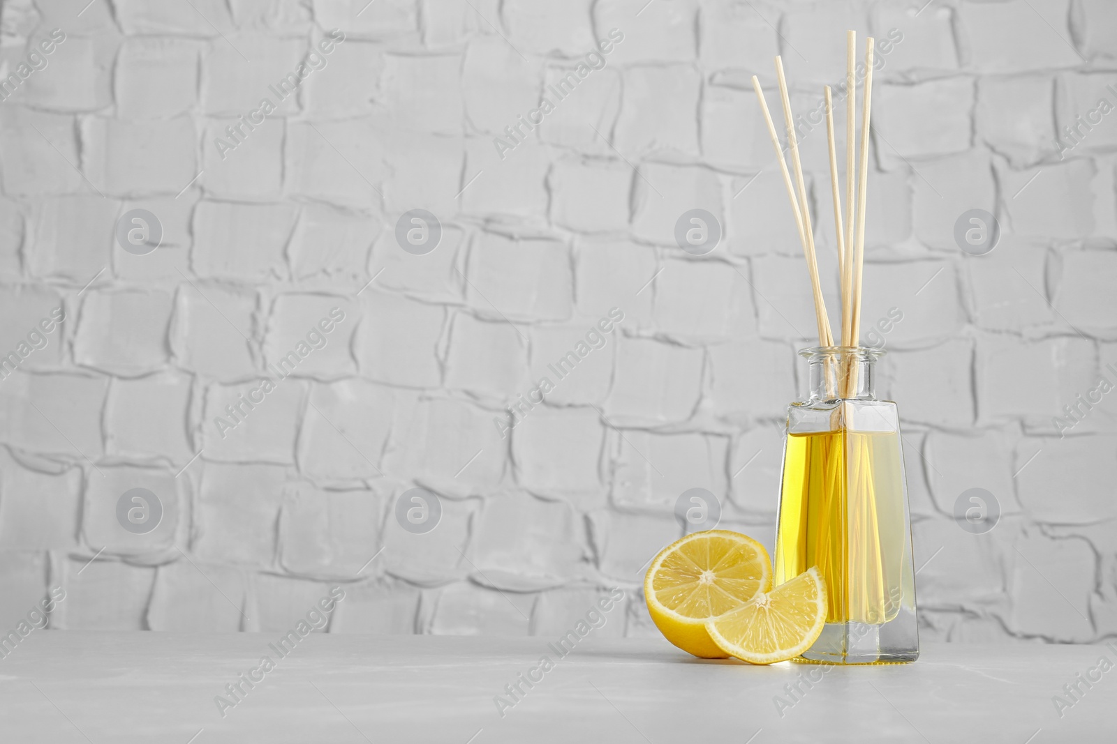 Photo of Aromatic reed freshener and lemon on table against textured wall. Space for text