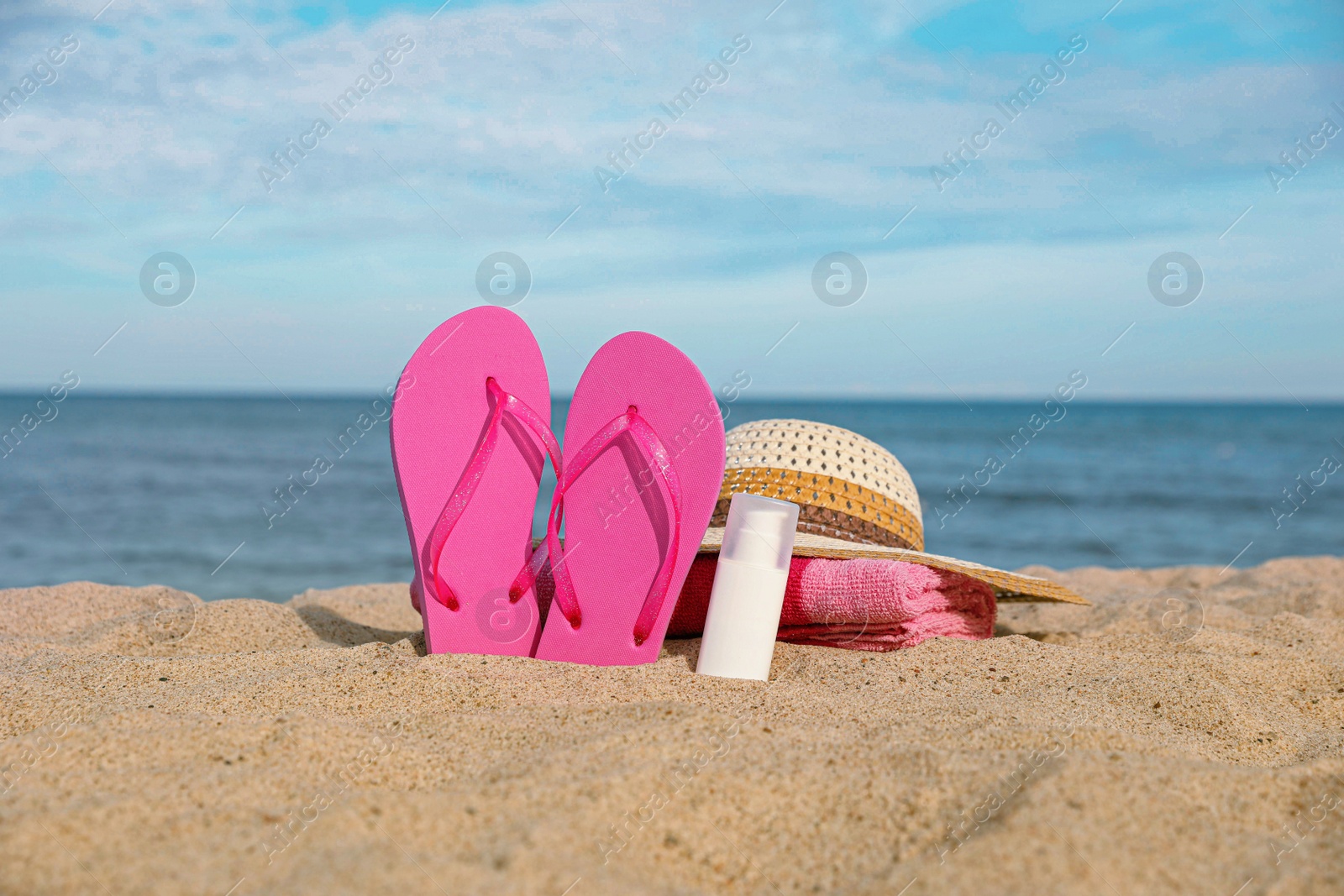 Photo of Beach towel, slippers, sunscreen and straw hat on sand near sea