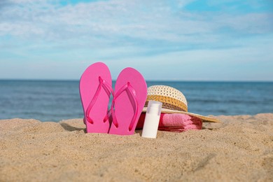 Photo of Beach towel, slippers, sunscreen and straw hat on sand near sea