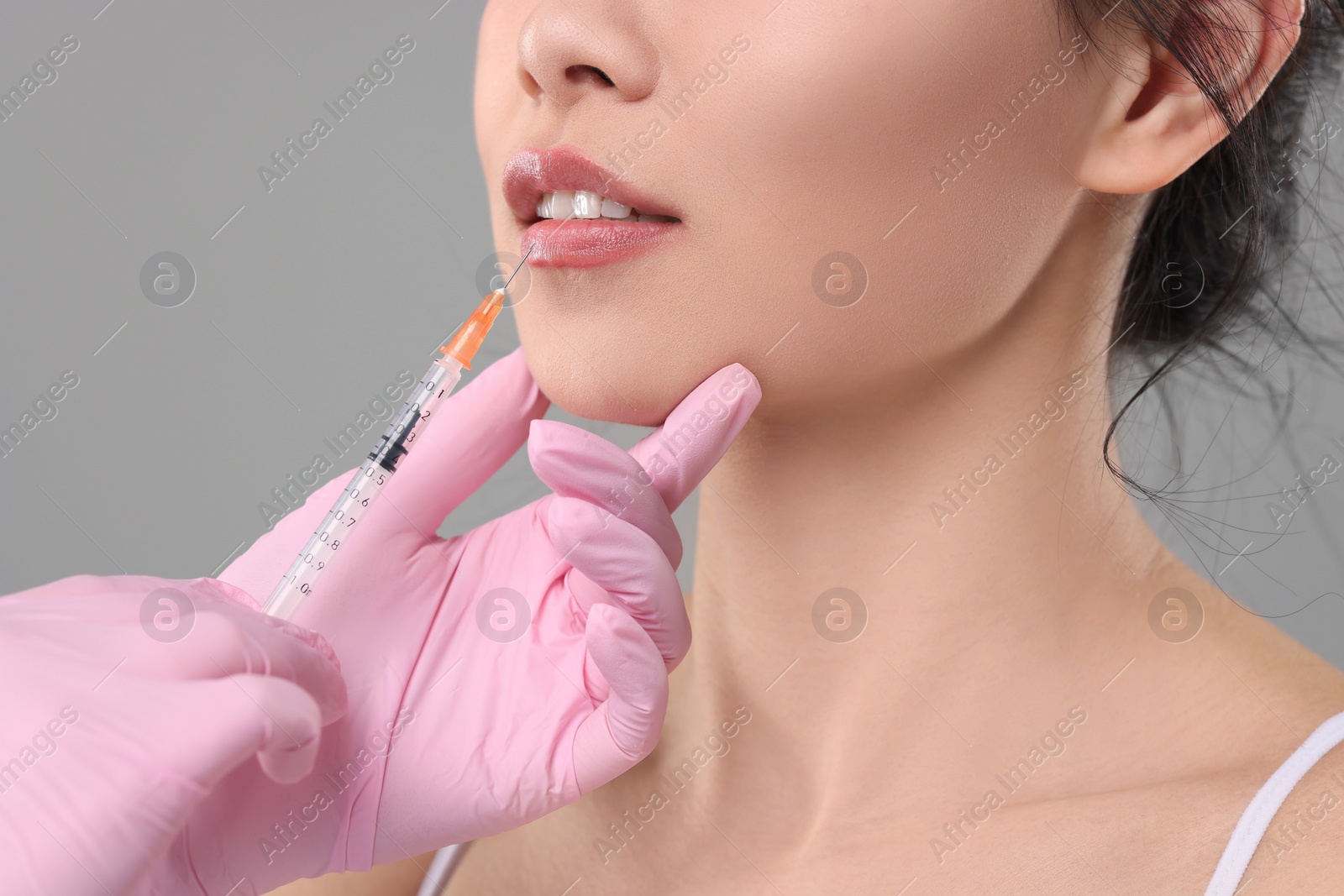 Photo of Woman getting lip injection on grey background, closeup