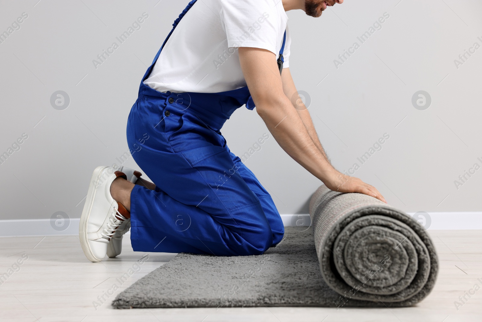 Photo of Worker unrolling new carpet on floor in room, closeup