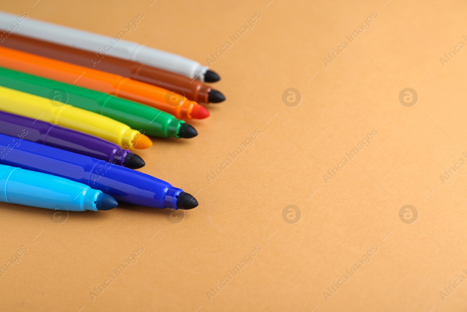 Photo of Different colorful markers on light brown background, space for text