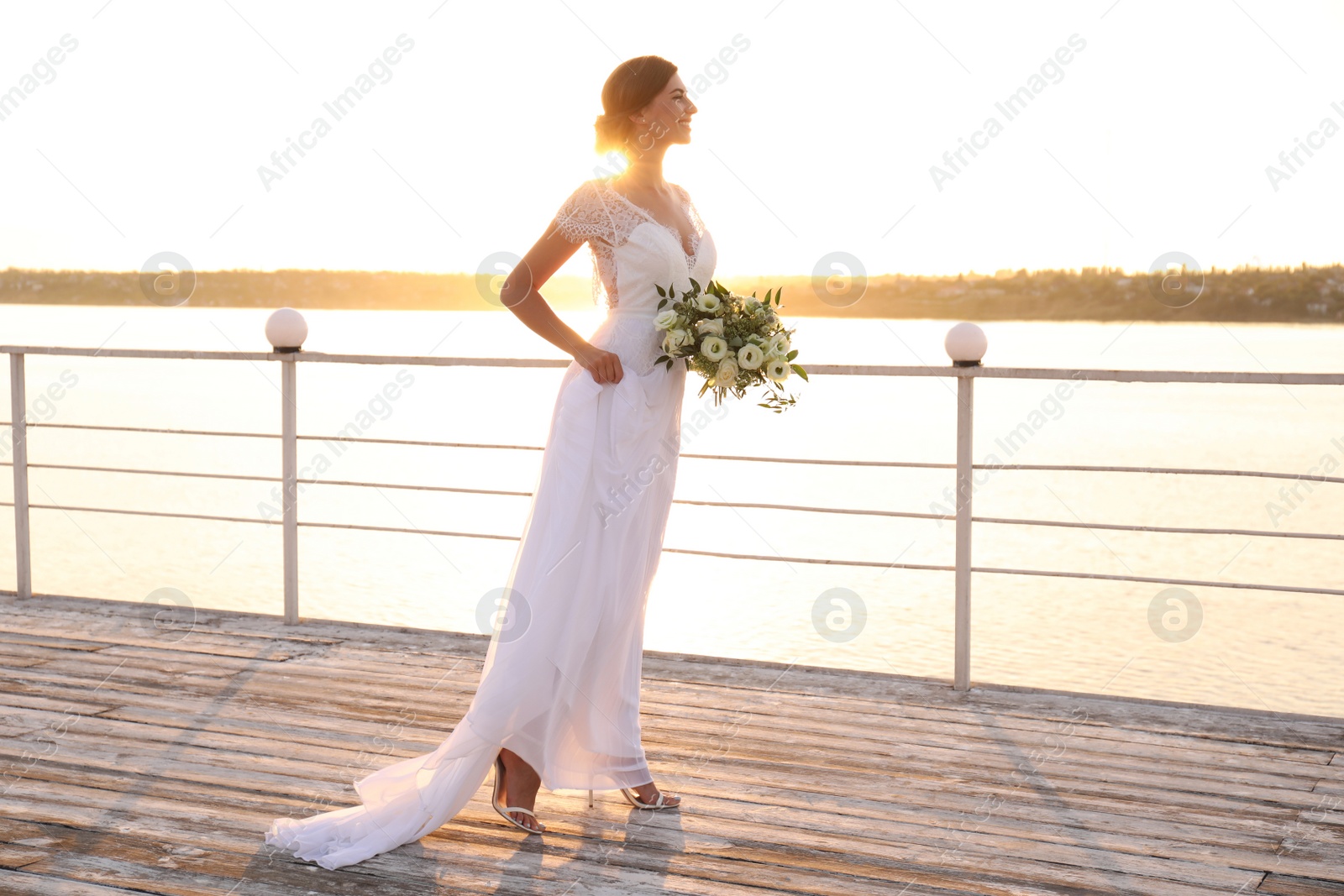 Photo of Gorgeous bride in beautiful wedding dress with bouquet near river on sunset