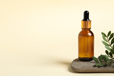 Photo of Bottle with cosmetic oil, stone and green leaves on beige background, space for text