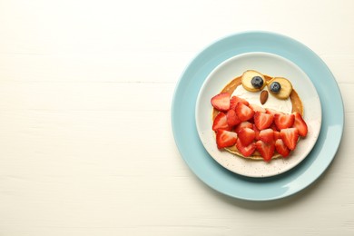 Creative serving for kids. Plate with cute owl made of pancakes, strawberries, cream, banana and almond on white wooden table, top view. Space for text