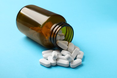 Photo of Bottle and vitamin capsules on light blue background