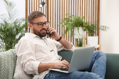 Photo of Young man talking on phone while working with laptop at home