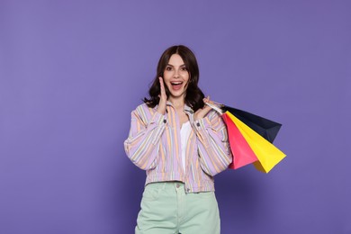 Emotional young woman with paper shopping bags on purple background