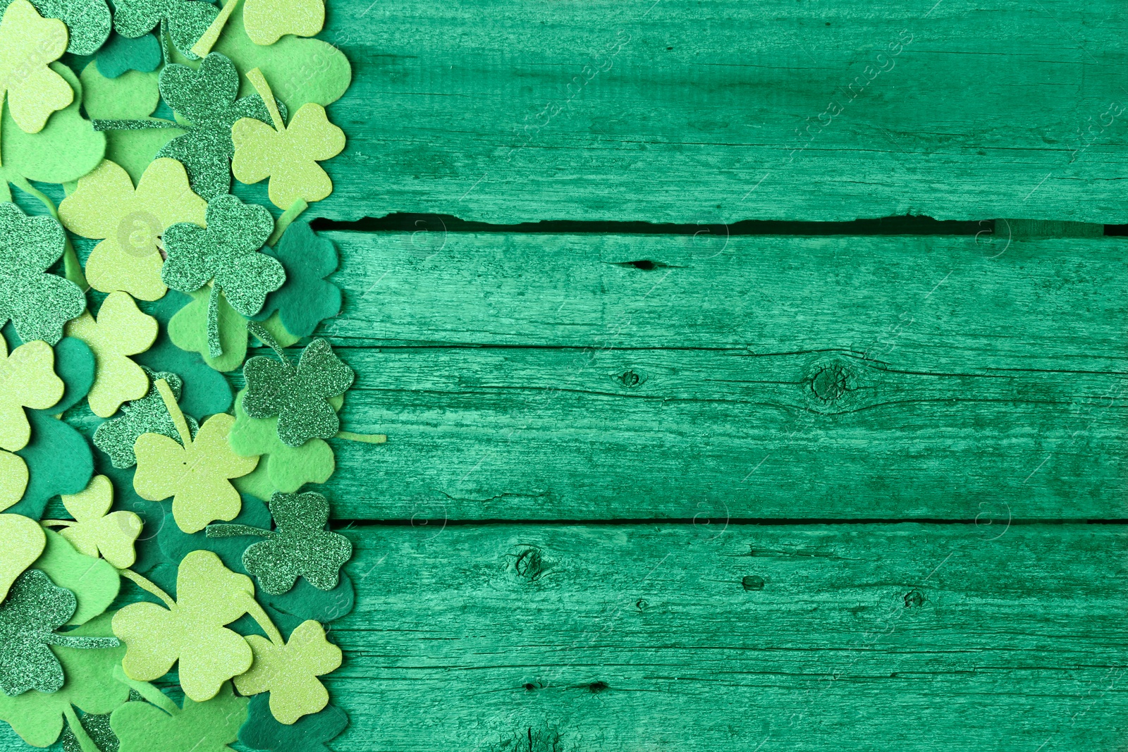 Image of St. Patrick's day. Decorative clover leaves on green wooden background, top view. Space for text