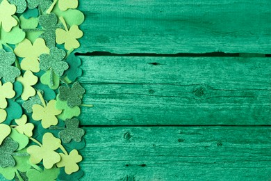 Image of St. Patrick's day. Decorative clover leaves on green wooden background, top view. Space for text