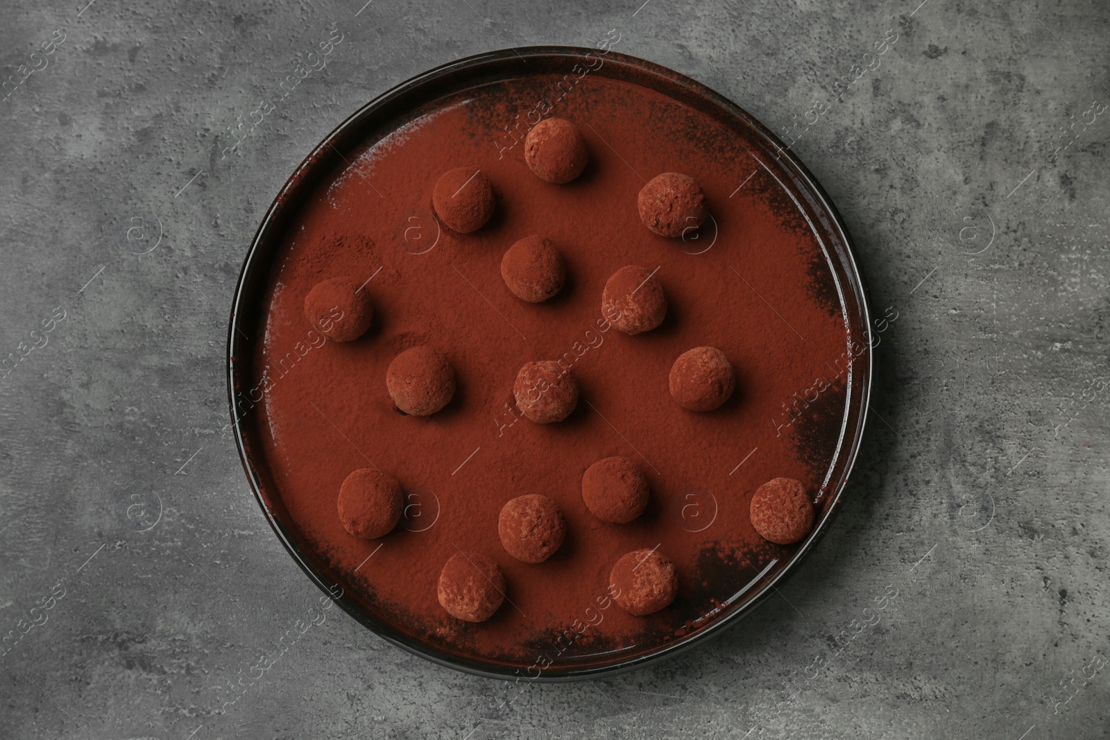 Photo of Delicious chocolate candies powdered with cocoa on grey table, top view
