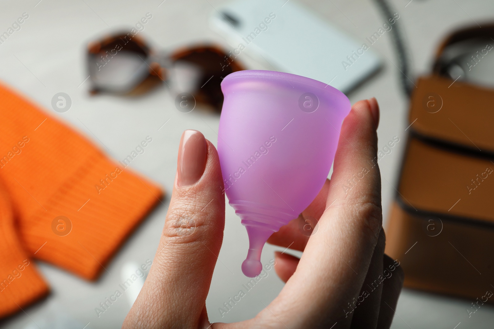 Photo of Woman holding violet menstrual cup on blurred background, closeup