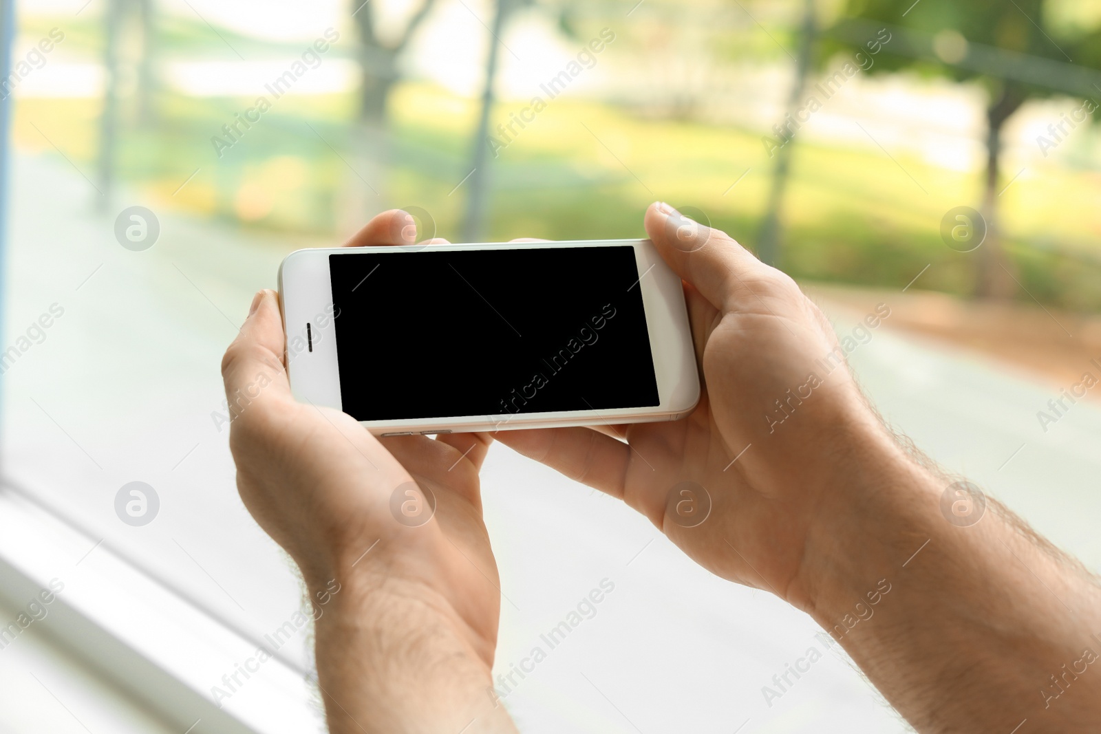 Photo of Man holding mobile phone with blank screen on blurred background, closeup. Mockup for design