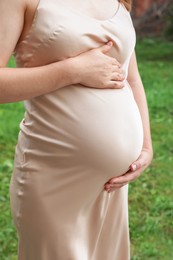 Photo of Pregnant woman touching belly outdoors, closeup view