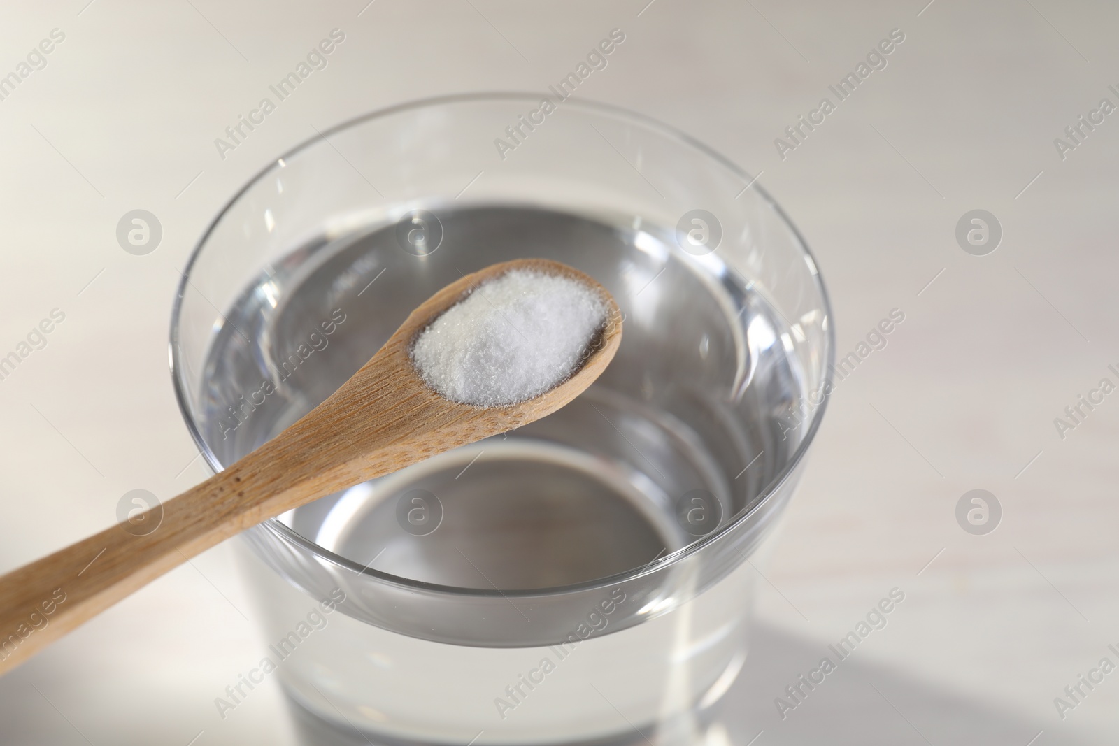 Photo of Spoon with baking soda over glass of water on light background, closeup