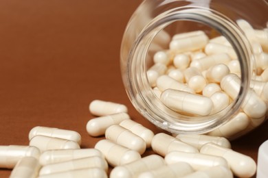 Photo of Open medicine bottle with pills on brown background, closeup