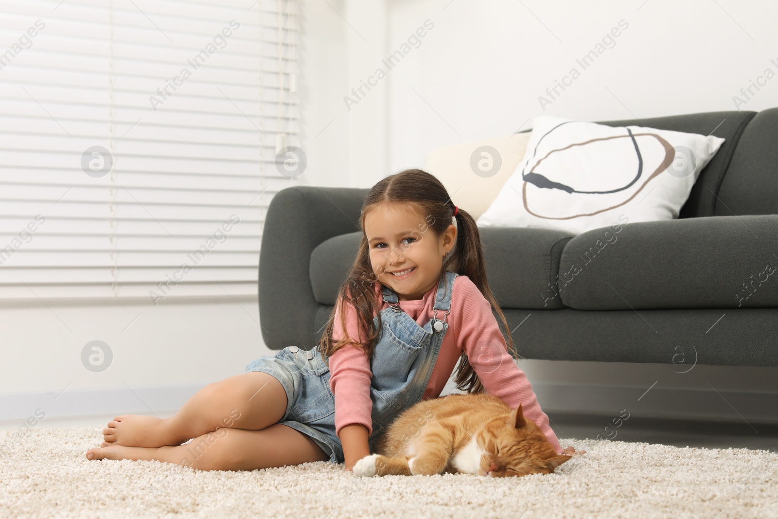 Photo of Happy little girl and cute ginger cat on carpet at home