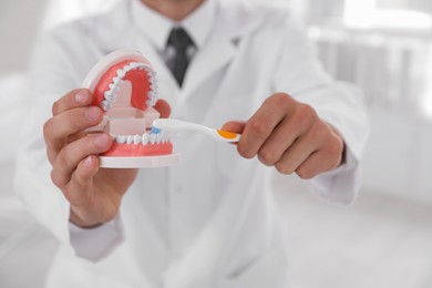 Photo of Dentist with jaws model and toothbrush in clinic, closeup. Oral care demonstration
