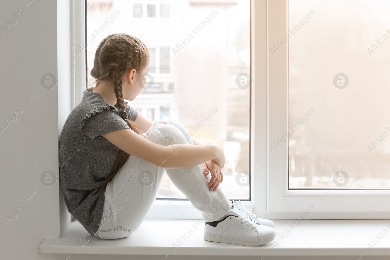 Photo of Lonely little girl near window indoors. Child autism
