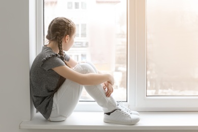 Lonely little girl near window indoors. Child autism