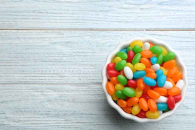 Photo of Bowl with colorful jelly beans on white wooden background, top view. Space for text