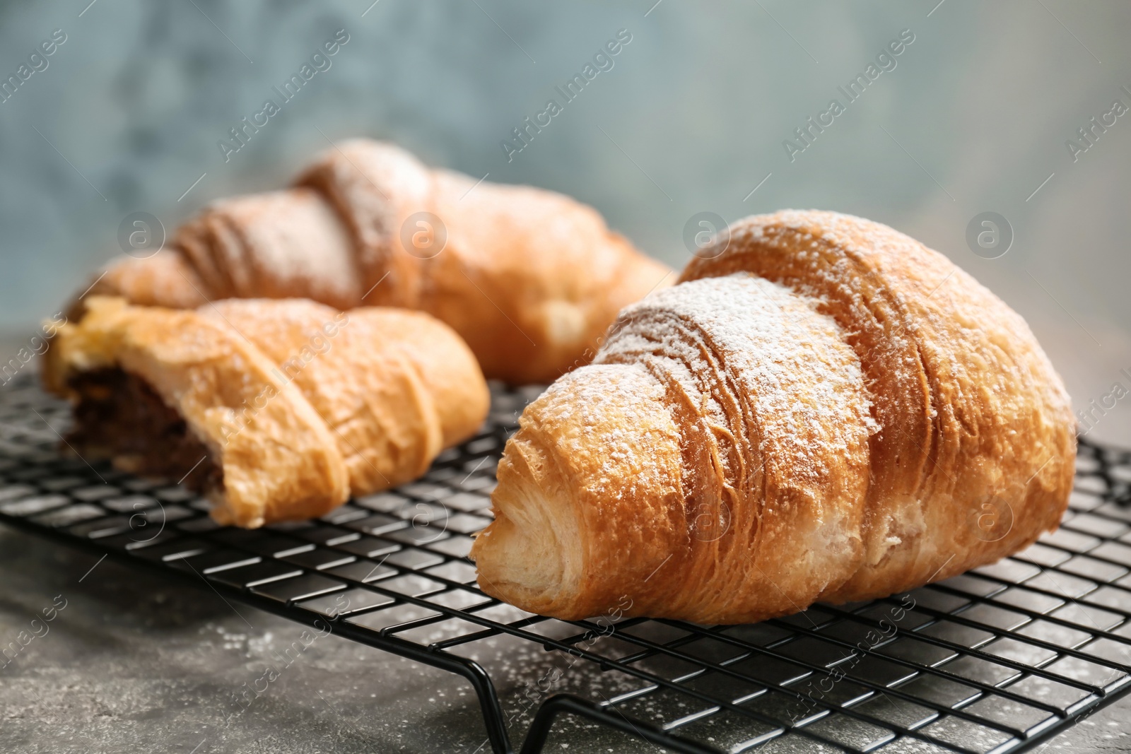 Photo of Tasty croissant with sugar powder on cooling rack