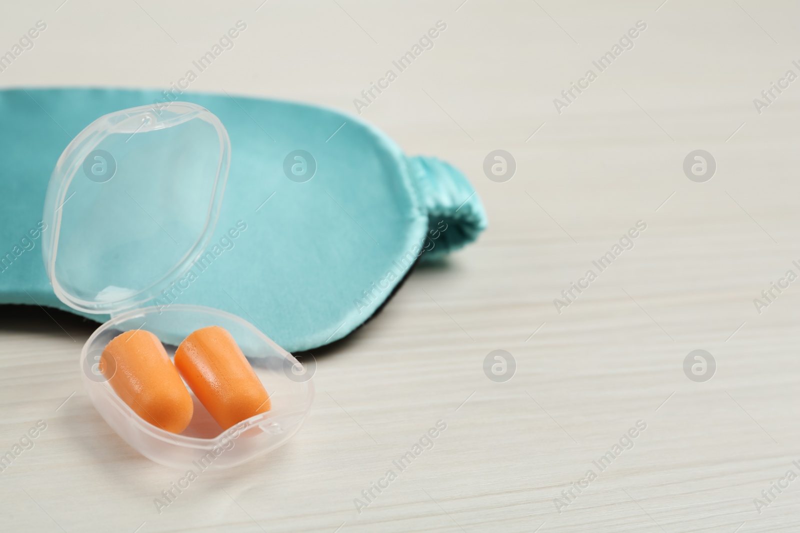 Photo of Pair of ear plugs and sleeping mask on white wooden background. Space for text