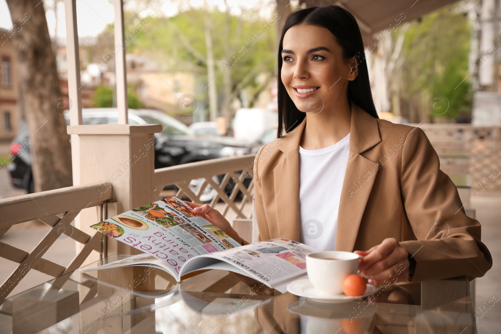 Photo of Woman with cup of coffee reading magazine at outdoor cafe in morning