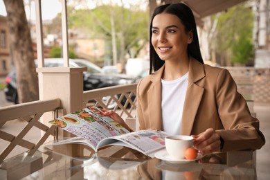 Woman with cup of coffee reading magazine at outdoor cafe in morning