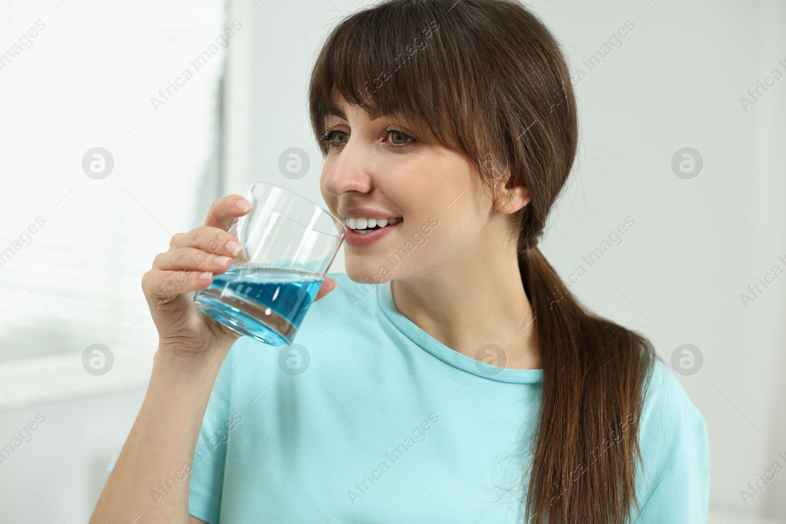 Photo of Young woman using mouthwash in bathroom. Oral hygiene