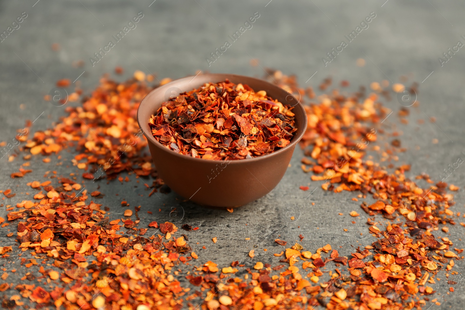 Photo of Bowl with chili pepper flakes on grey background