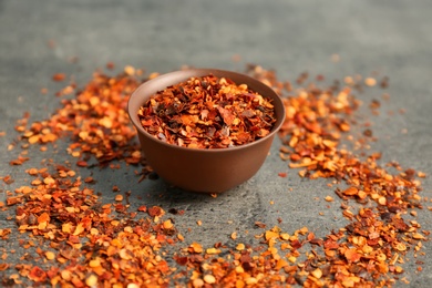 Photo of Bowl with chili pepper flakes on grey background