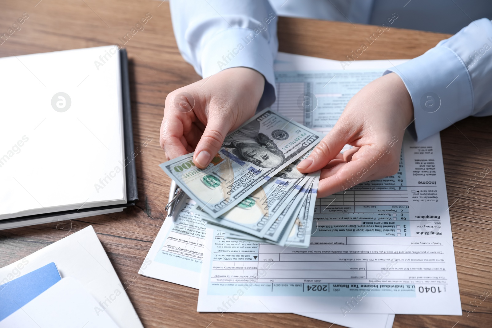 Photo of Payroll. Woman with dollar banknotes and tax return forms at wooden table, closeup