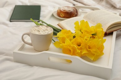 Bouquet of beautiful daffodils and hot drink on bed