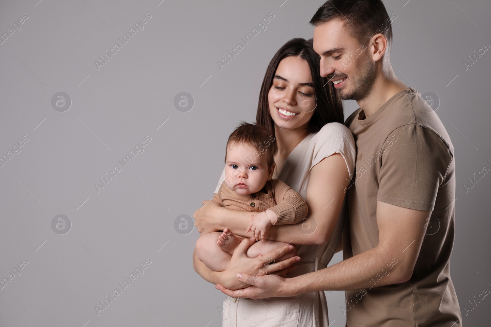 Photo of Happy family. Couple with their cute baby on grey background, space for text