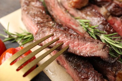 Photo of Fork with delicious grilled beef on table, closeup