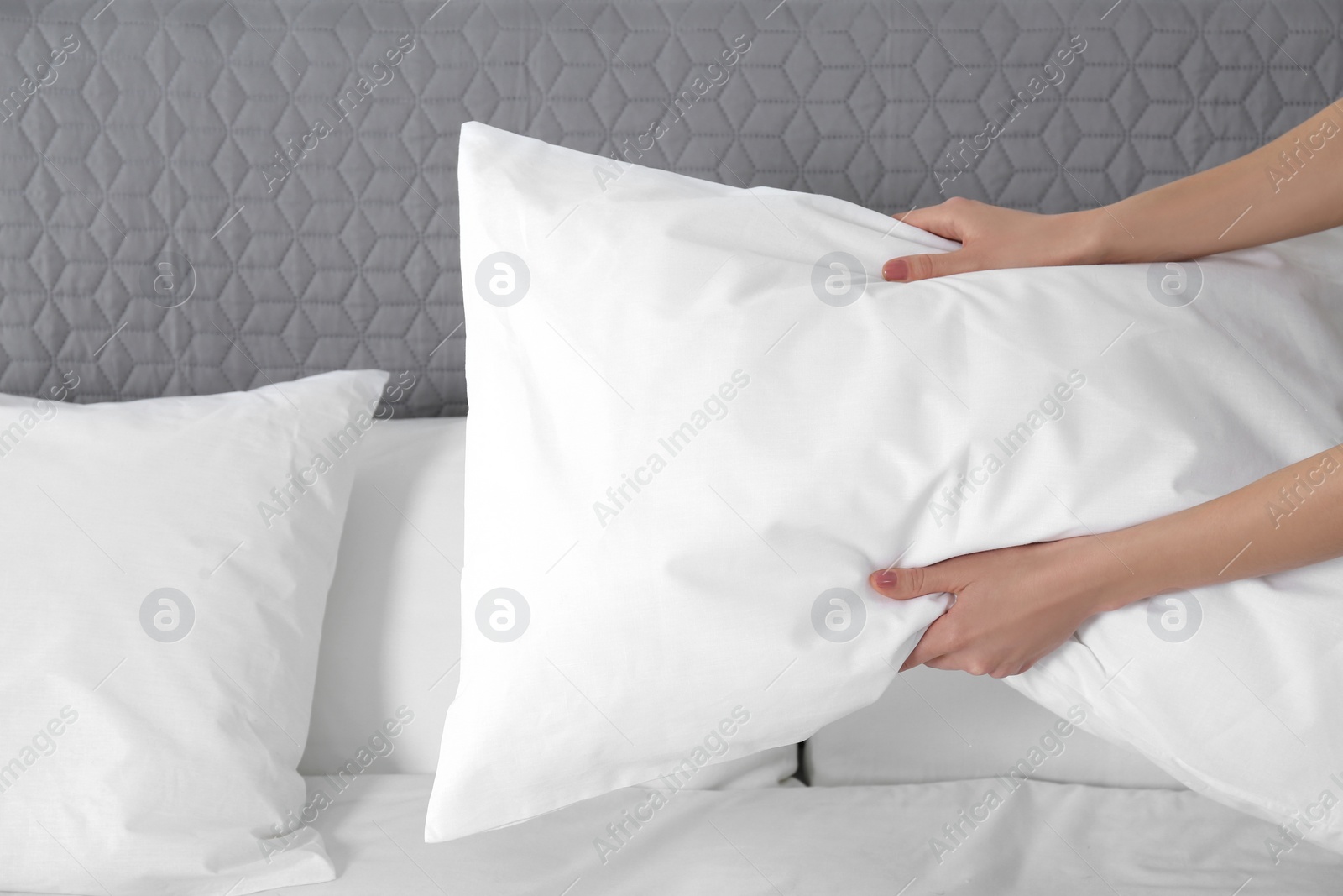 Photo of Woman fluffing soft pillow in bedroom, closeup