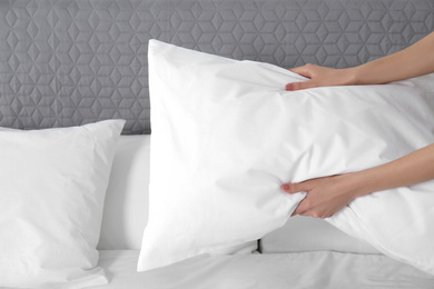 Photo of Woman fluffing soft pillow in bedroom, closeup